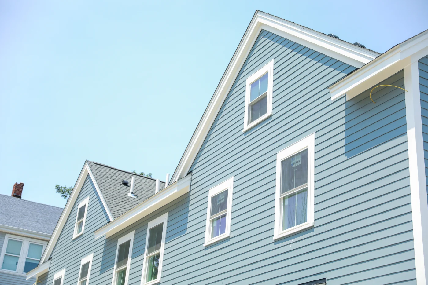 The back side of a home in daylight, covered in light blue siding. The house has a light gray shingled roof, white window trim and gutters.