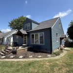 A home with blue siding and a dark gray roof. There are multiple steps leading up to the front door, and a large garden bed that runs along the front of the home