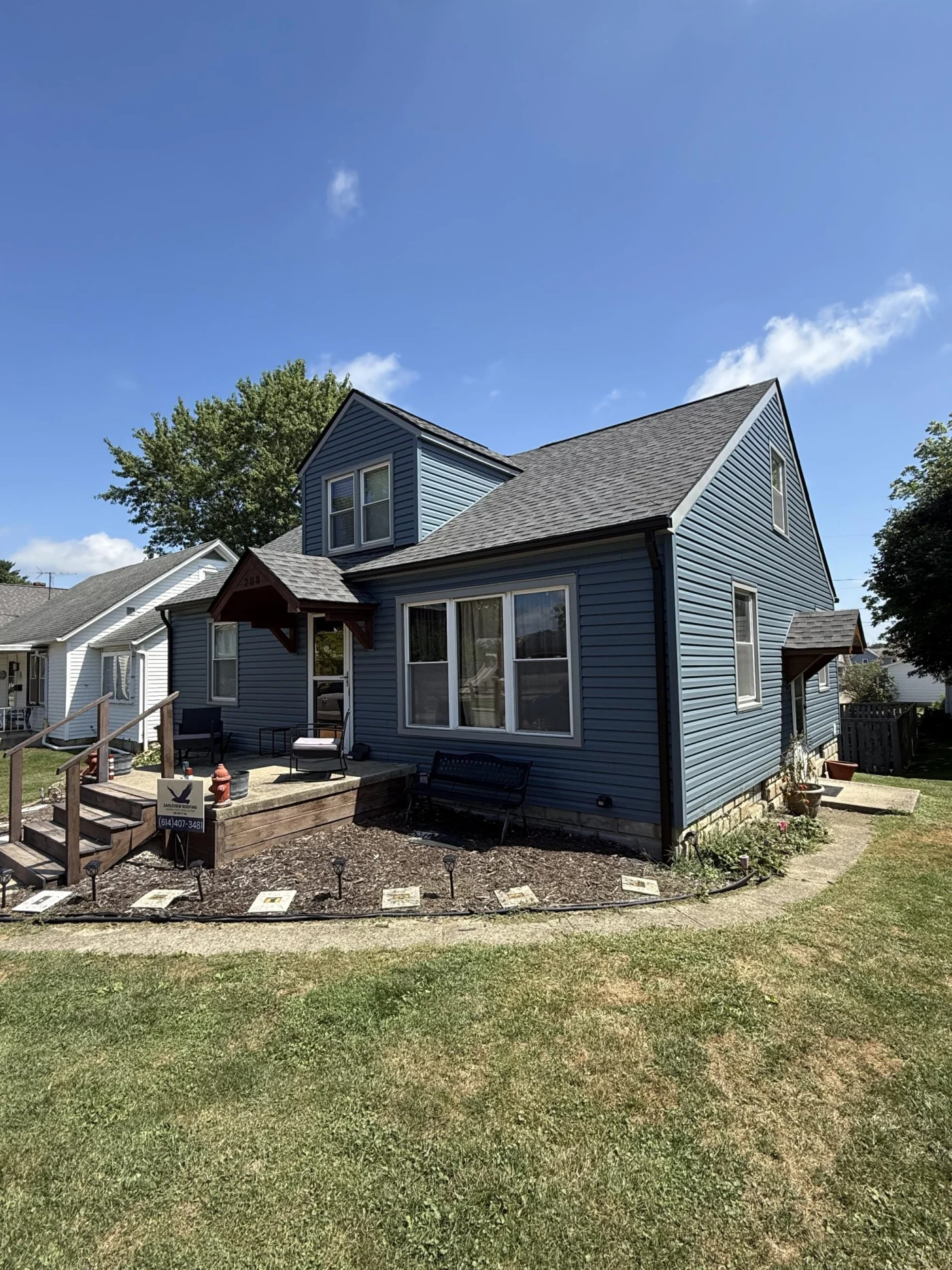 A home with blue siding and a dark gray roof. There are multiple steps leading up to the front door, and a large garden bed that runs along the front of the home